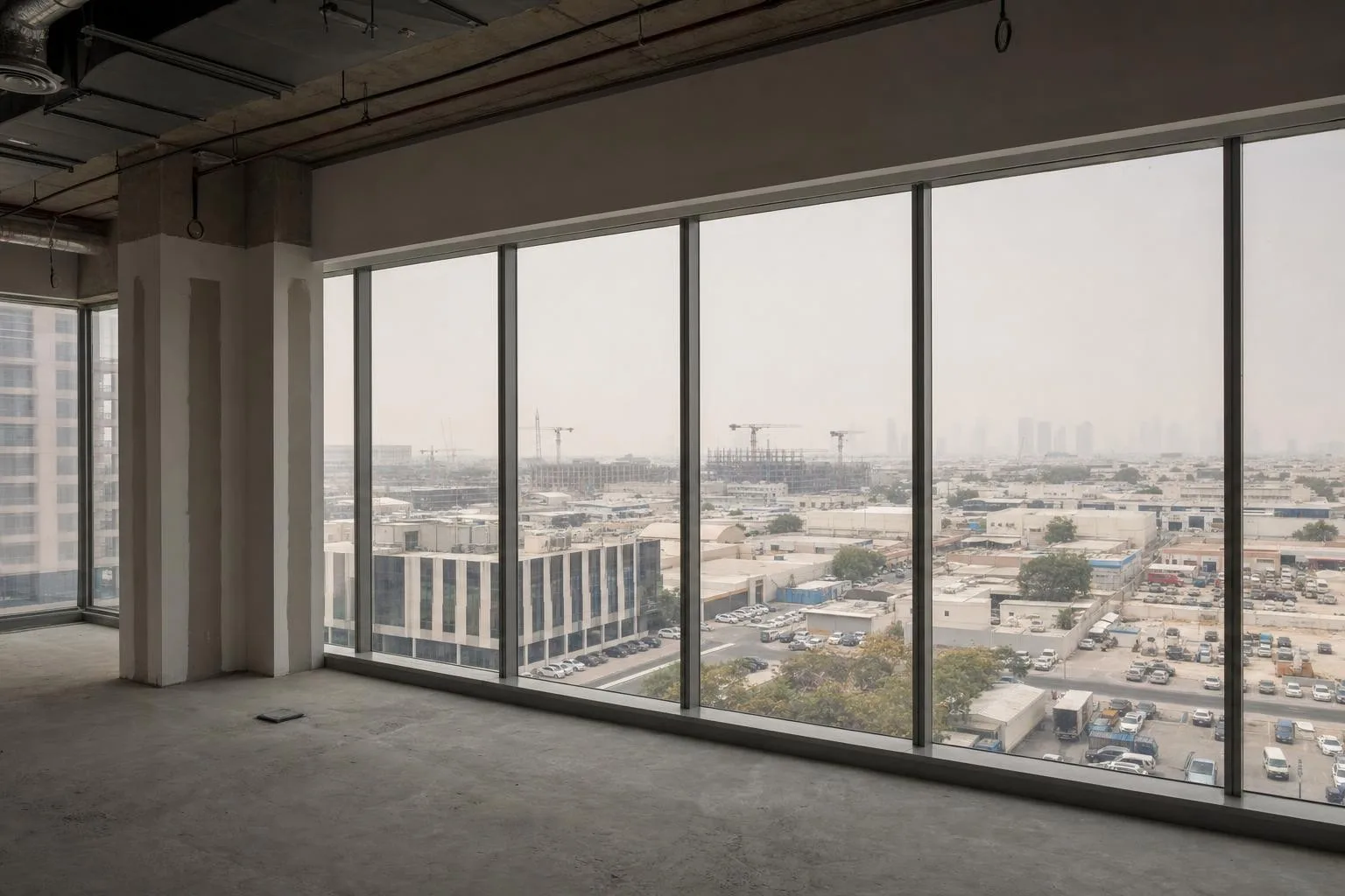 An unfinished floor plate in a Dubai commercial building, looking out over a working district in morning haze